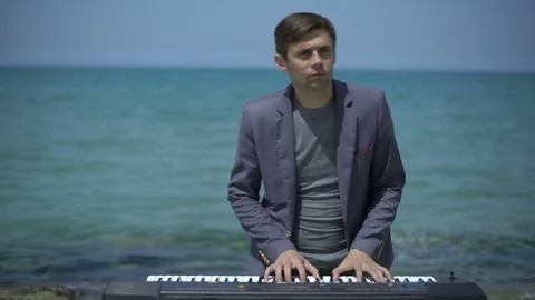 Young man performs witm synthesizer on azure coast, beach or quay. Hands Stock Footage 80333432