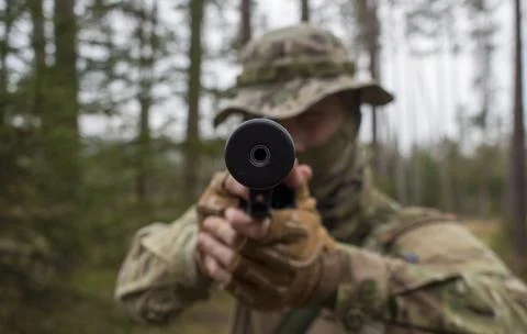 A young man (perhaps a soldier) fires a short silenced firearm. Stock Photos