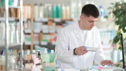 Young man pharmacist uses computer at workplace. Colleague work in background Stock Footage 317992156