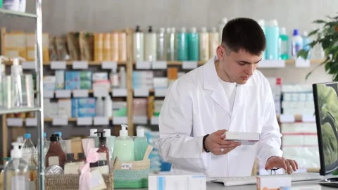 Young man pharmacist uses computer at workplace. Colleague work in background Stock Footage 331295122