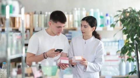 Young man in pharmacy scans QR code on tablets, pharmacist in background Stock Footage 323912588