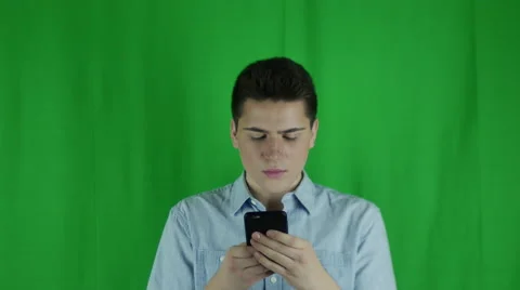 Young man is on phone and looks up annoyed waves off in front of a greenscreen Stock Footage 59083982