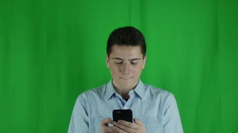 Young man is on phone and looks up looking confused in front of a greenscreen Vidéo 59084349