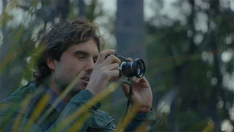 A young man with a photo camera talking a photograph in the forest Stock Footage 107247539