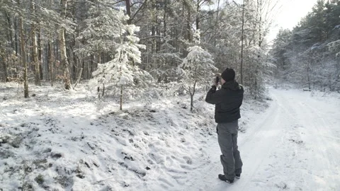 A young man is photographing a fur-tree in a winter forest. Stock Footage 85518617