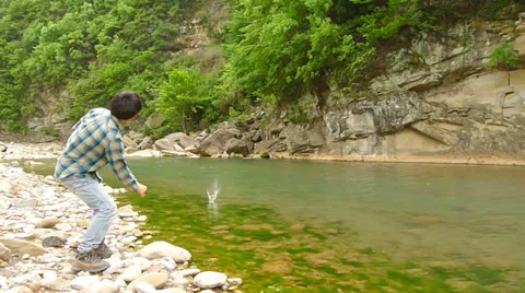 Young man picking up and skipping stones along a beautiful river Stock Footage 37771712
