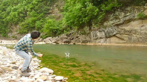 Young man picking up and skipping stones along a beautiful river Stock Footage 37771960