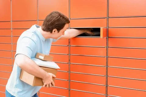 Young man picking up or dropping off packages at an automated orange parcel.. Stock Photos