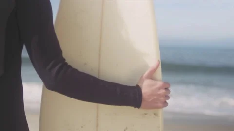Young man picks up his surfboard, and walks out of focus on a beach shore Vídeos de archivo 83020985
