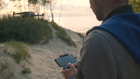 Young man piloting a drone at sunset flying out in forest near seacoast Stock Footage 219920540