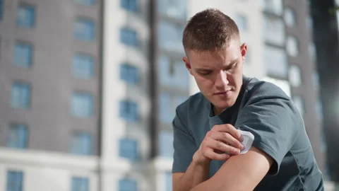 Young man placing nicotine patch on upper arm with residential building behind Stock Footage 307055783