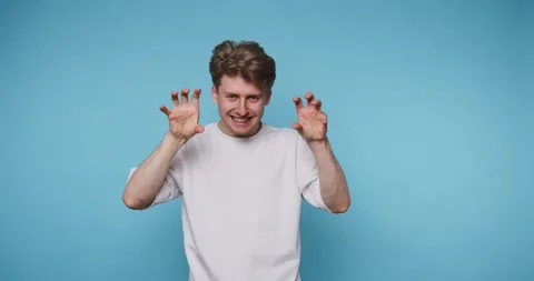 Young man playfully posing with claw hands on blue background. Stock Footage 315162323