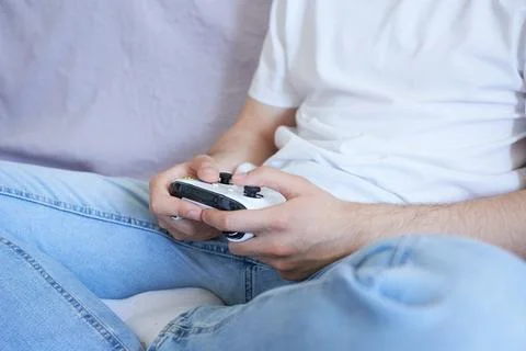 A young man is playing a console while sitting on the couch. Foto stock