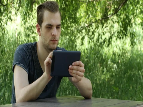 Young Man Playing with Digital Tablet Social Networking Wood Table Park Location Stock Footage 69872158