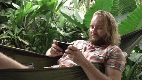 Young man playing game on mobile phone while sitting on hammock Video stock 84841050
