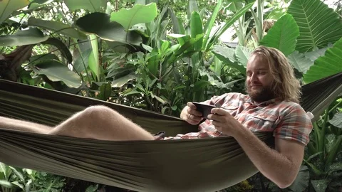 Young man playing game on smartphone while sitting on hammock Stock Footage 84818337