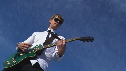 Young man playing guitar on against a blue sky Stock Footage 96516211