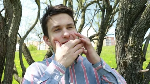 Young Man Playing Harmonica Under Blossoming Trees in a Spring Park Stock Footage 274134559