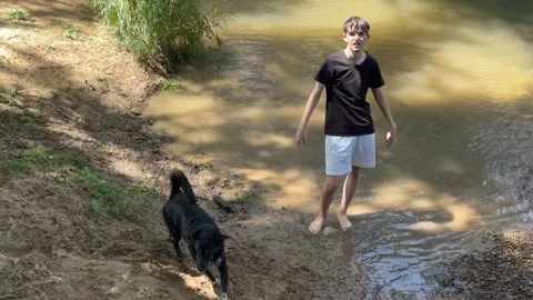 Young man playing with his dog in a muddy river Stock Footage 342344111