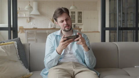 Young Man Playing Mobile Game On Smartphone With Intense Reaction Stock Footage 344697099