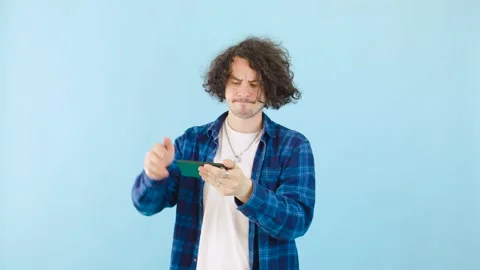 Young man playing mobile games and losing while standing against bright blue Stock Footage 281049168