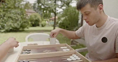 Young man playing outdoor backgammon in a sunny garden. Capturing leisure and Stock Footage 281576805