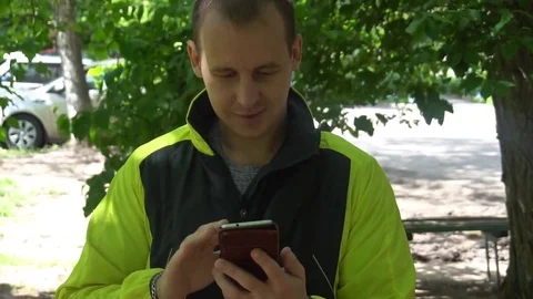 Young man playing the phone,in the background of green trees Stock Footage 75914631