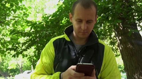 Young man playing the phone,in the background of green trees Stockbeeldmateriaal 75914851