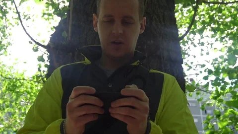 Young man playing the phone,in the background of green trees Stock Footage 75914969