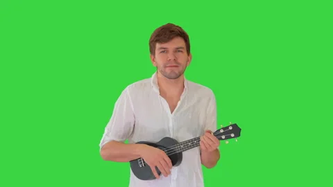 Young man playing ukulele and signing while walking and looking into camera on a 動画素材 138595459