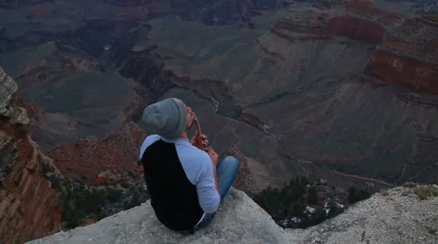 Young man playing ukulele at the edge of a rock at Grand Canyon Stock Footage 65326392