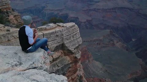 Young man playing ukulele at the edge of a cliff at Grand Canyon Stock Footage 65326423