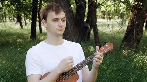 Young man playing a ukulele in a field and sings energetically. Young hipster 動画素材 108389562