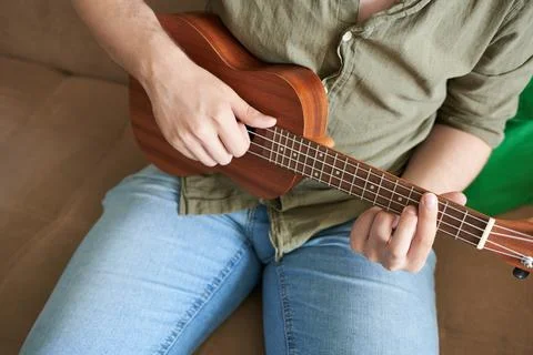 Young man playing ukulele on sofa at home, closeup Stock Photos
