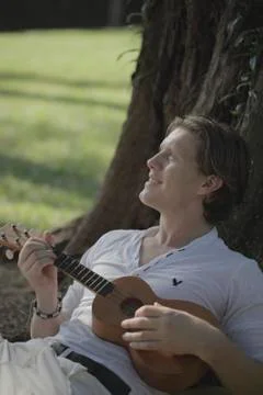 Young man playing ukulele under a tree Stock Photos