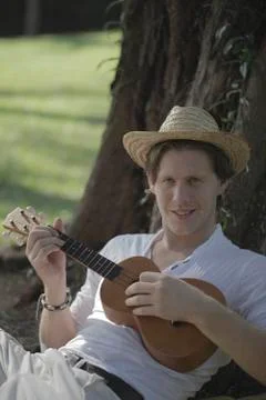 Young man playing ukulele under a tree Stock Photos