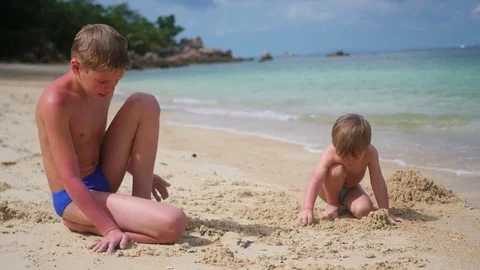 A young man plays with child on the beach. To make the sand molds Vidéo 75865091