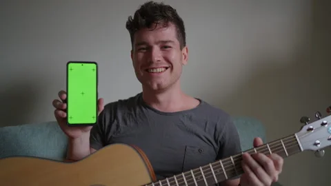 Young man plays guitar learns from smartphone app. Smartphone screen with green Stock Footage 298732636