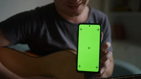 Young man plays guitar learns from smartphone app. Smartphone screen with green Stock Footage 303555423
