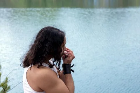 Young man plays on harmonica on the river bank. Stock Photos