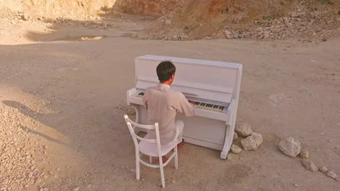 Young man plays the piano on a background of yellow mountains and stones Stock Footage 90912341