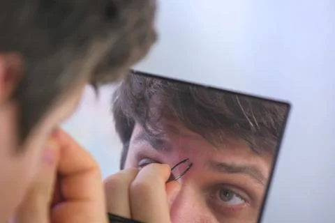 Young man plucks his eyebrows with tweezers in front of the mirror at home. Stock Illustration