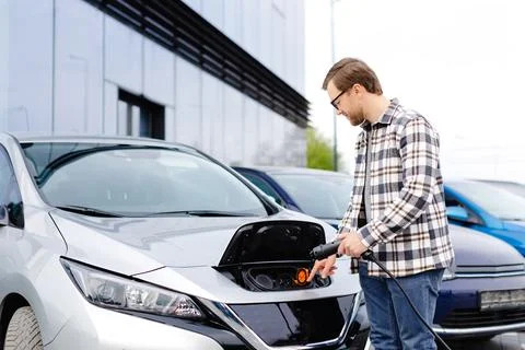 Young man plugging charging cable into the car socket. Electric car chargin.. Stock Photos