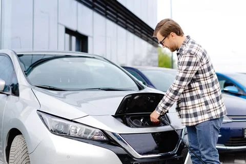Young man plugging charging cable into the car socket. Electric car chargin.. Stock Photos