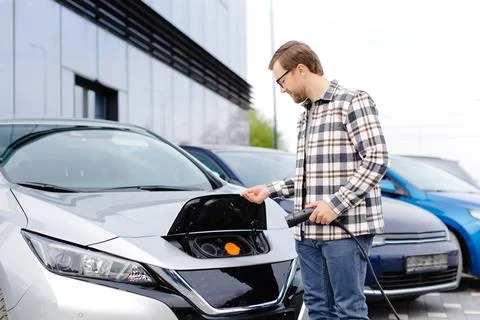 Young man plugging charging cable into the car socket. Electric car chargin.. Stock Photos