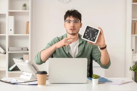 Young man pointing at clock showing six oclock, time management and deadline  Stock Photos