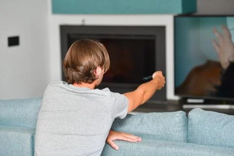 Young man pointing a remote control at an out of focus television on an out o Stock Photos