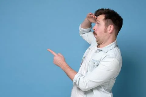 Young man pointing, surprised by something or someone, isolated on blue Stock Photos
