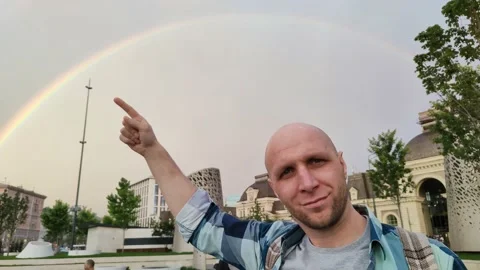 Young man points his finger at rainbow after rain 스톡 동영상 201636094