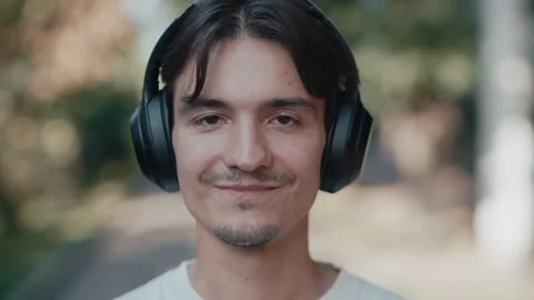 Young man portrait smiling while listening to music with headphones outdoors Stock Footage 339215642